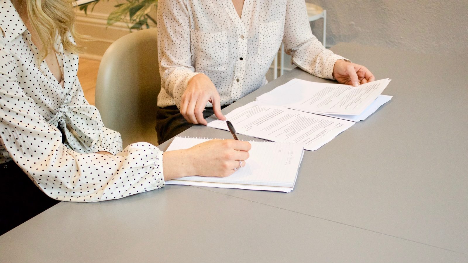 woman signing on white printer paper beside woman about to touch the documents